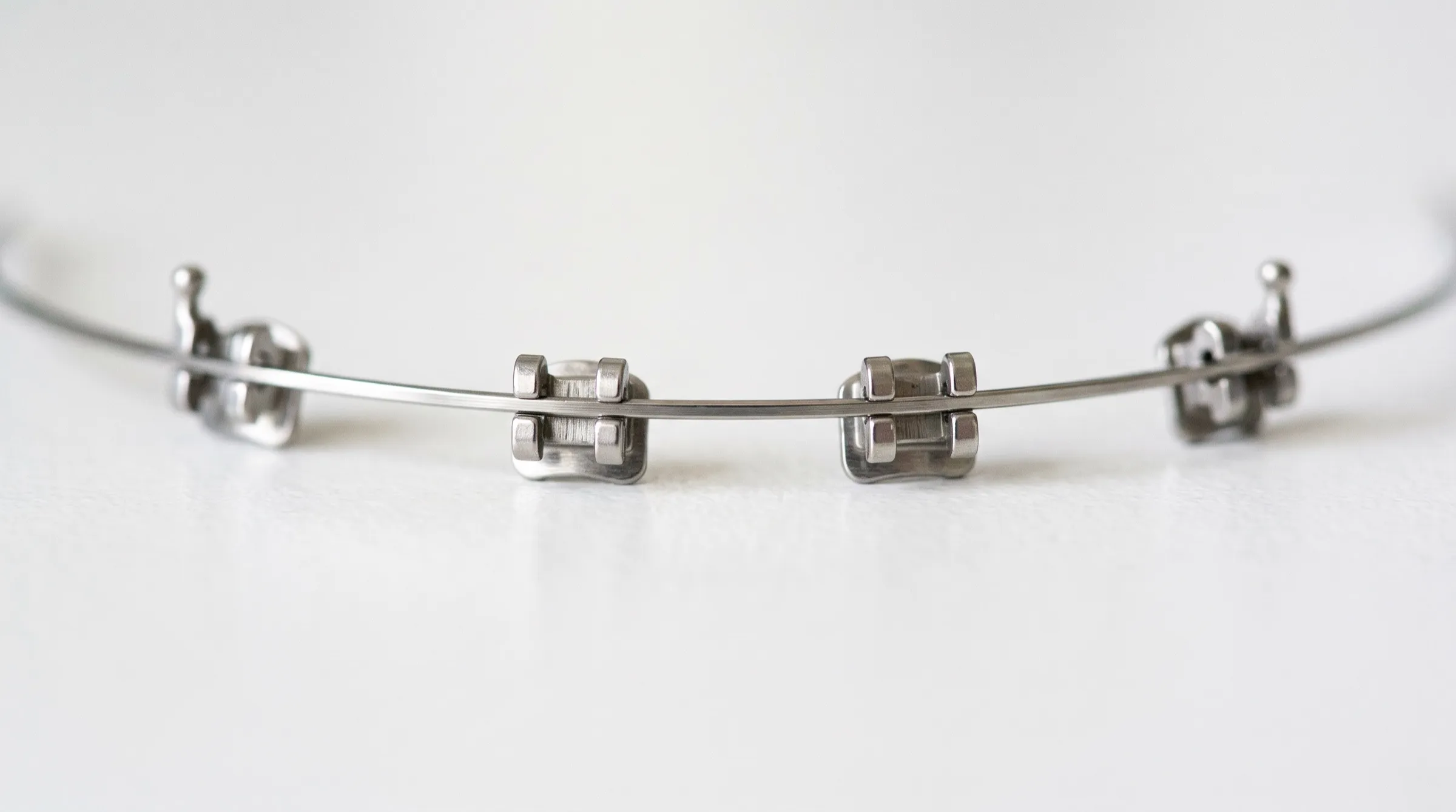 Illustrative macro photograph of a polished orthodontic archwire resting across a row of metal brackets on a white bench.
